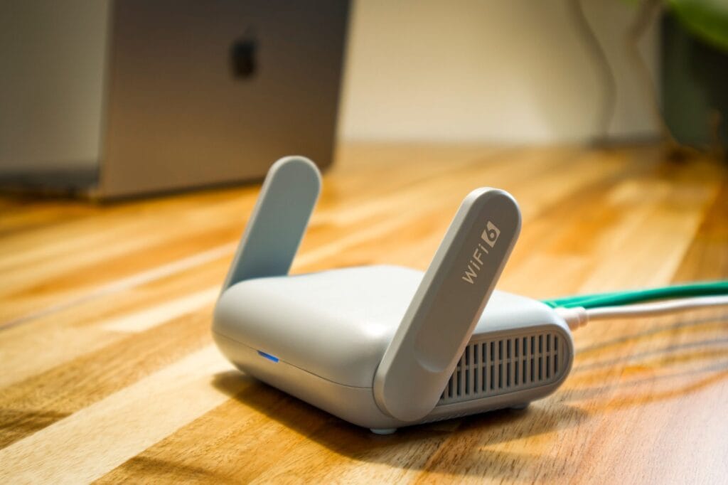 A WiFi 6 router with antennas and ethernet cable on a wooden desk next to a laptop, representing home network requirements for Chromecast casting.