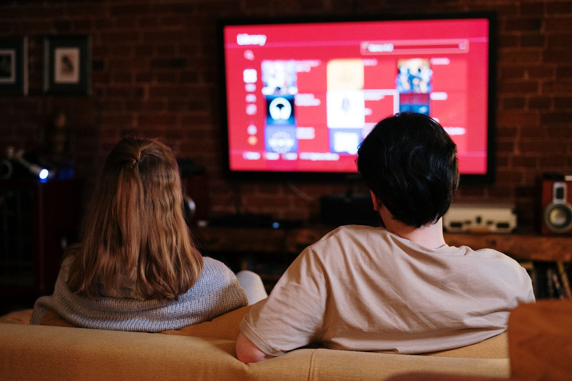 A couple sitting on a sofa watching a large TV streaming content in a cozy brick-walled living room, representing movie night via Chromecast from PC.