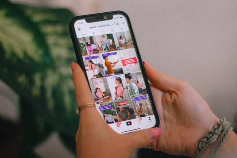 Person holding a smartphone showing a TikTok-style social media grid feed, representing social content creation on mobile