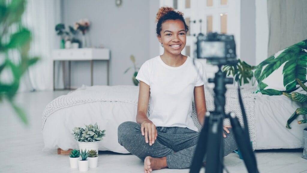 8 Free iPhone Video Editing Apps: No Watermark Test Female content creator sitting cross-legged on the floor recording a video for social media, with a camera on a tripod in front of her